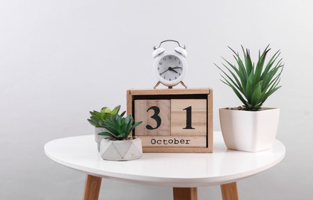 Wooden calendar organizer with date October 31 and decorative plants, alarm clock on table