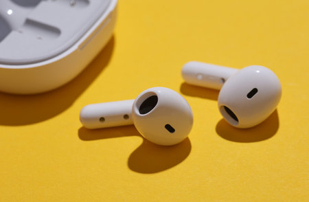 Wireless earphones with charging case on yellow background.