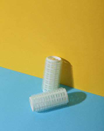 Plastic hair curlers on yellow and blue background. Beauty concept, creative layoutの写真素材