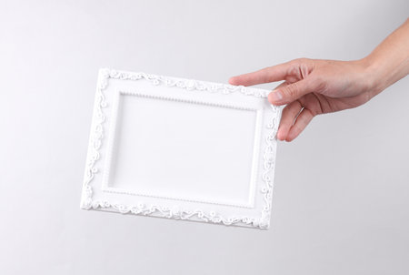Hand holding white blank Ornamental photo frame on gray background