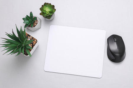 Mockup of white blank computer mouse pad with props, decorative plants on gray background. Top view....