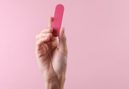 Female hand holding nail file on pink backgroundの写真素材