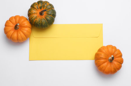 Miniature natural pumpkins with envelope on white background. Autumn still life. Halloween theme. Top view. Copy spaceの写真素材