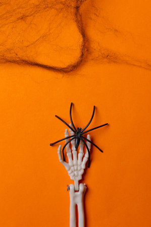 Skeleton hand with spider and web on orange background