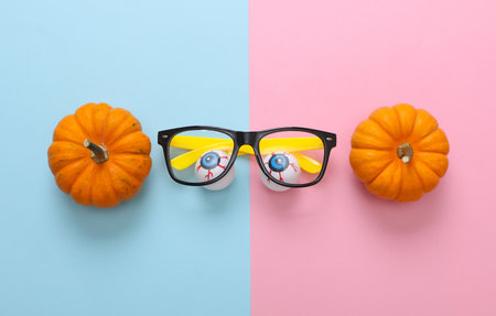 Eyeballs with eyeglasses and pumpkins on pink blue background. Halloween still lifeの写真素材