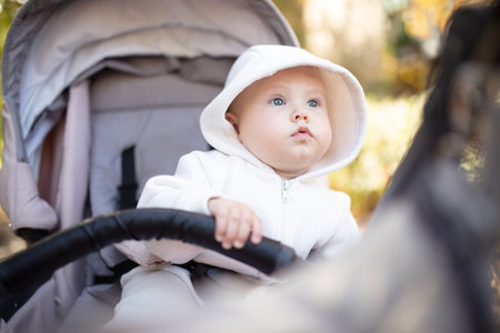 Little cute baby in hoodie sits in stroller outdoors