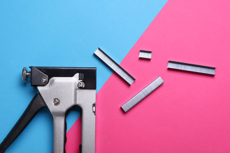 Construction stapler with staples on a pink blue background