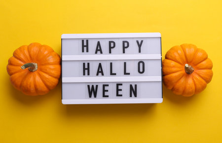 Happy Halloween letterboard text on LED Lightbox and pumpkins, yellow background. Flat layの写真素材
