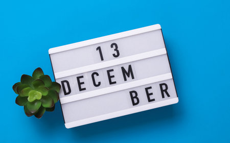 Lightbox with text December 13 on blue backgroung with decorative plant. Flat lay. Top viewの写真素材