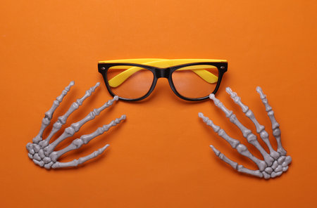 Halloween decoration concept. Plastic skeleton hands and eyeglasses on orange background. Flat layの写真素材
