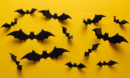 Halloween decoration concept. Black paper bats flying on yellow background. Top view