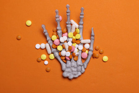 Skeleton hand with pills on orange background. Halloween, medicine conceptの写真素材