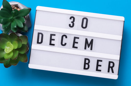 Lightbox with text December 30 on blue backgroung with decorative plant. Flat lay. Top viewの写真素材