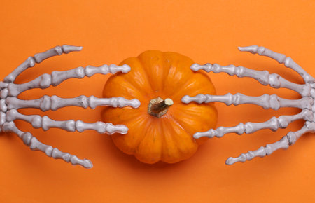 Halloween decoration concept. Plastic skeleton hands with pumpkin on orange backgroundの写真素材