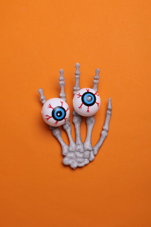 Halloween decoration concept. Plastic skeleton hand holding eyeballs on orange background
