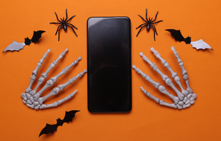 Halloween decoration concept. Plastic skeleton hands and smartphone on orange backgroundの写真素材
