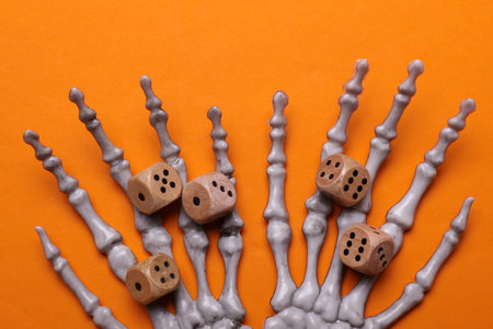 Skeleton hands with dice on orange background.