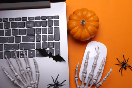 Skeleton hands using laptop with halloween decor on orange background. Top viewの写真素材