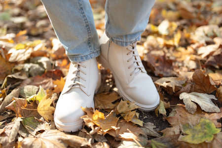Female legs in light jeans and white leather boots. Woman walking in autumn park during daytime with...
