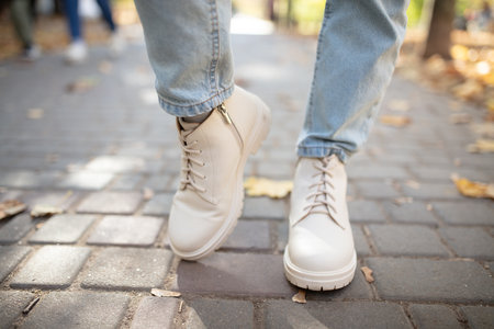 Female legs in light jeans and white leather boots. Woman walking in autumn park during daytime with fallen leavesの写真素材