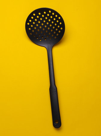 Black kitchen spatula colander on yellow backgroundの写真素材