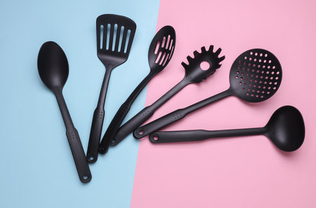 Black plastic kitchen tools on pink blue background. Top view. Flat lay