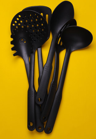 Black plastic kitchen tools on yellow background. Top view. Flat lay