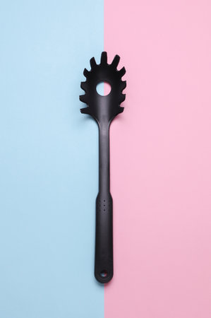 Black plastic kitchen tool on pink blue background