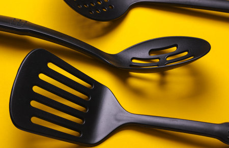 Black plastic kitchen tools on yellow background. Top view. Flat layの写真素材