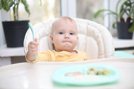 Cute little baby eats food from a plate at a tableの写真素材