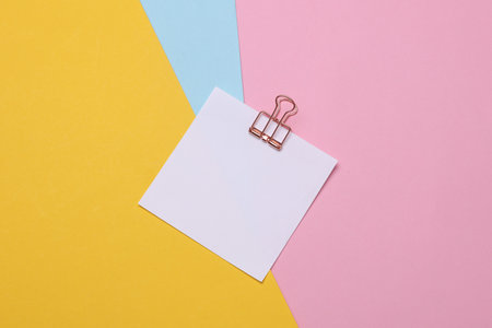 Memo white square sheet of paper with binder clip on colored background. Stationery, education,...