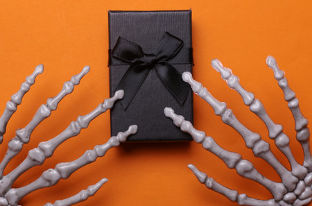 Halloween gifts concept. Gift box and skeleton hands on orange backgroundの写真素材