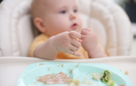 Cute little baby eats food from a plate at a tableの写真素材
