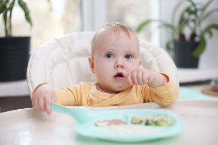 Cute little baby eats food from a plate at a tableの写真素材