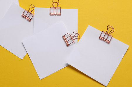 Memo white square sheets of paper with binder clips on yellow background. Stationery, education, business conceptの写真素材