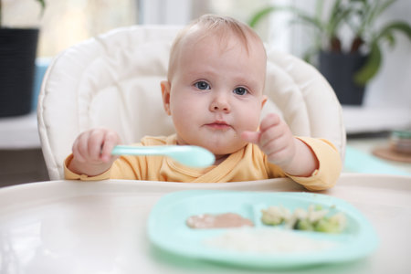 Cute little baby eats food from a plate at a tableの写真素材