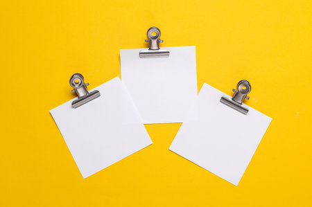 Memo white square sheets of paper with binder clips on yellow background. Stationery, education, business conceptの写真素材