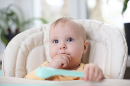 Cute little baby eats food from a plate at a tableの写真素材