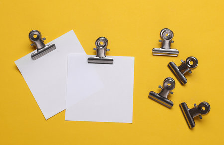 Memo white square sheets of paper with binder clips on yellow background. Stationery, education, business conceptの写真素材