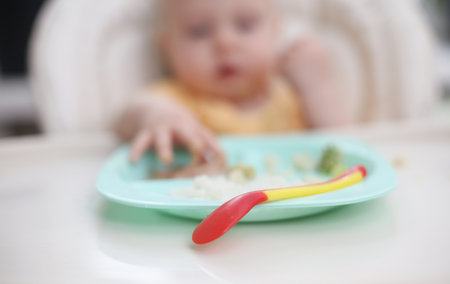 Cute little baby eats food from a plate at a tableの写真素材
