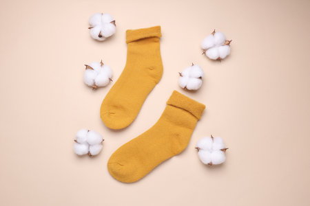 Yellow socks with cotton flowers on beige background. Natural clothing materials
