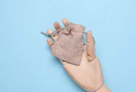 Wooden hand of puppet holding mini burlap bag on blue background