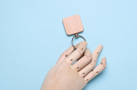 Puppet hand holding wooden keychain on blue backgroundの写真素材