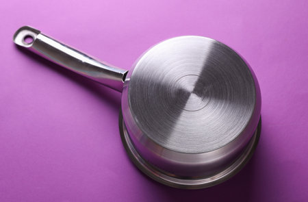 Metal saucepan with handle on purple background