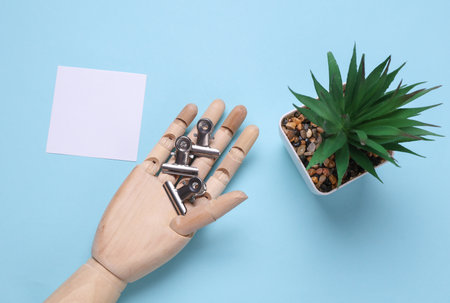 Wooden hand of puppet holding metal paper clip holders on blue background