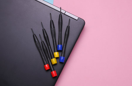 Laptop with screwdrivers on pink background. Repair of digital equipment and gadgets.