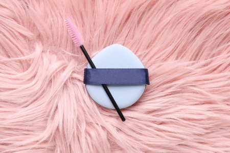 Makeup blender sponge and eyelash brush on pink fluffy background