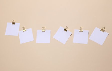 White blank square memo paper cards with gold binder clips on beige background. Mockup for design