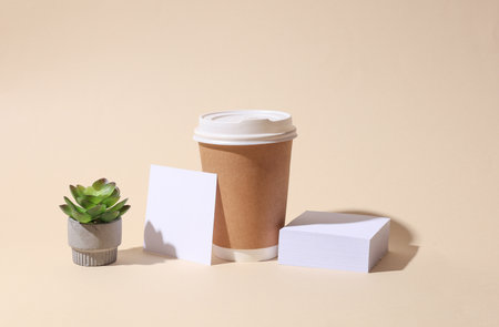 Craft cardboard disposable coffee cup and white square memo card on beige background with shadow....