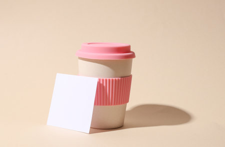 Plastic coffee cup and square white memo card on beige background with shadow